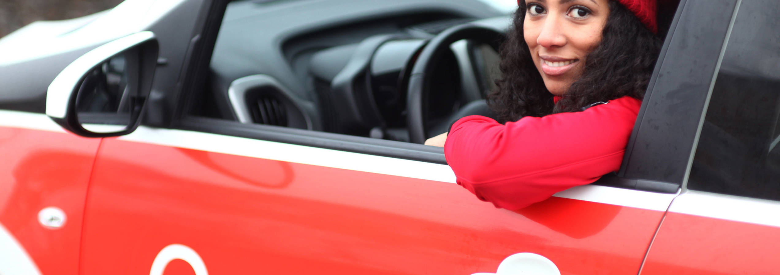 Caritas Altenpflegerin lächelt aus dem Autofenster heraus | © Caritas München