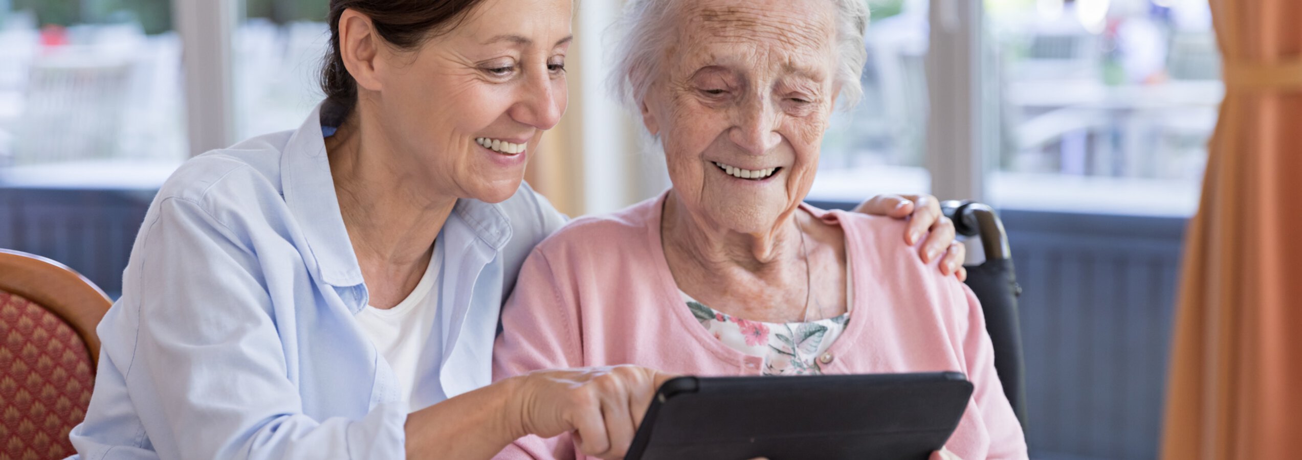 Caritas Altenpflegerin zeigt einer Seniorin etwas auf einem Tablet | © FredFroese/Getty Images